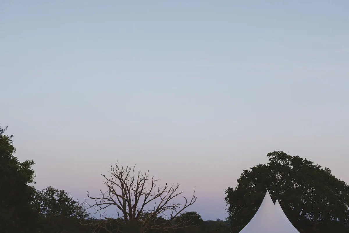 White marquee peak silhouetted against a soft dusk sky with tree outlines at a Dorset summer wedding