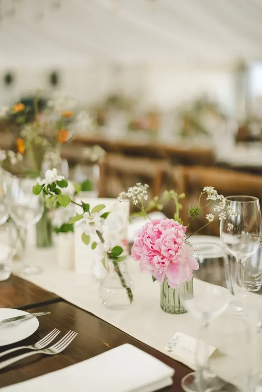 Marquee wedding reception table with pink peony and wildflower bud vases on dark wood trestle
