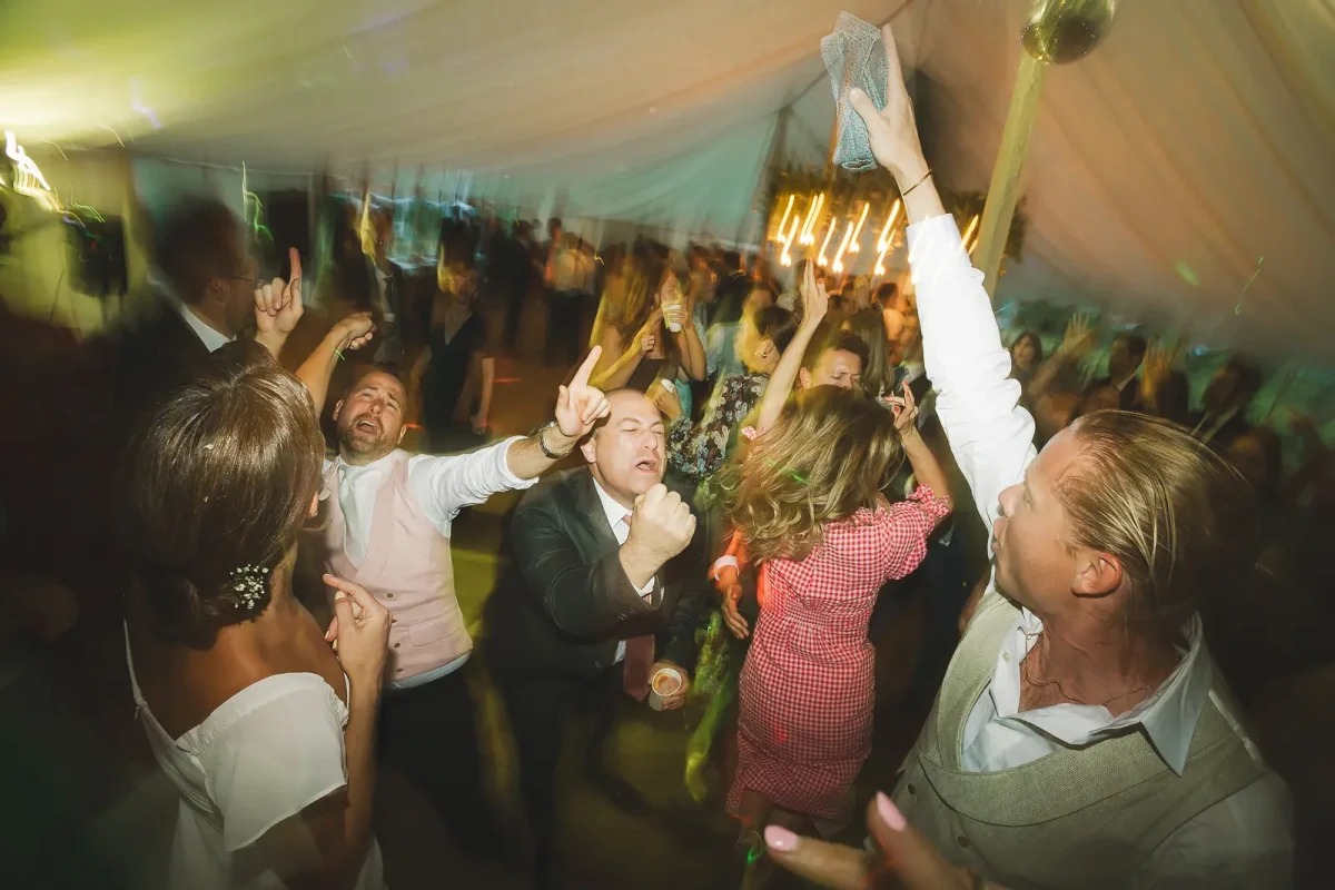 Packed marquee dance floor with wedding guests dancing wildly under warm lights during the evening party