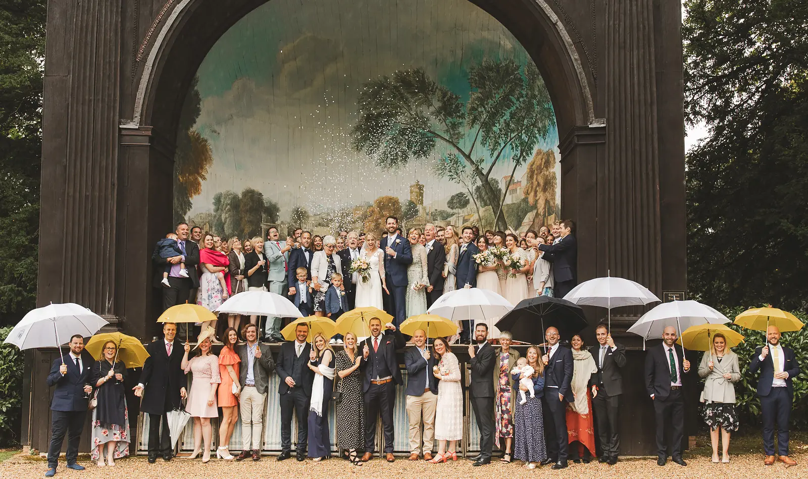 Wedding group photo with guests under umbrellas on a rainy wedding day in Dorset