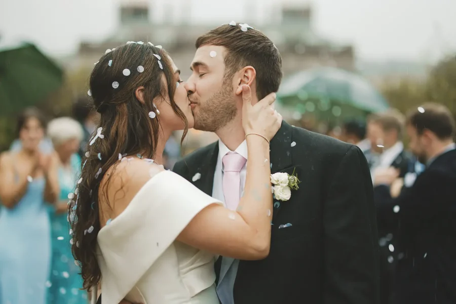 Bride and groom kissing during a rainy wedding moment with confetti in Dorset