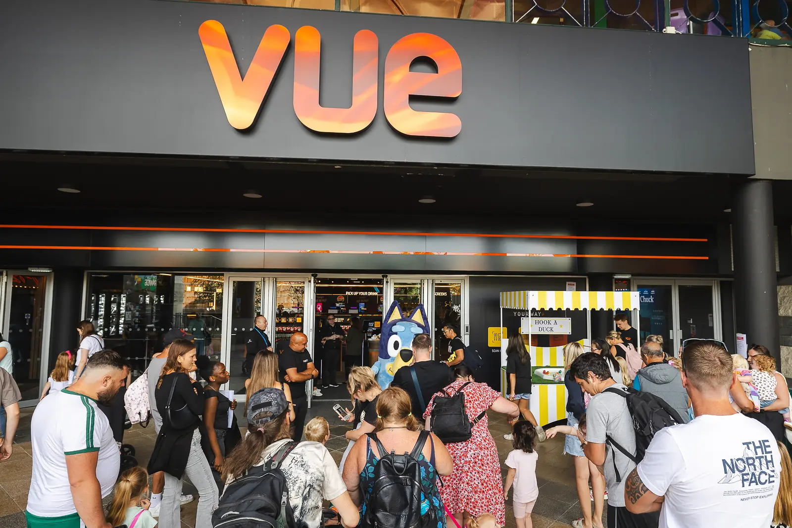 Large crowd of families gathered outside a venue entrance at a summer public event in Poole, with a costumed character visible in the doorway