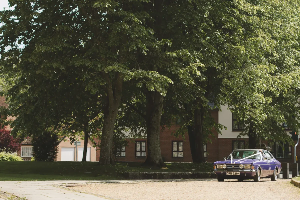 Vintage purple wedding car parked on the green near Wimborne Minster church on a sunny summer wedding day