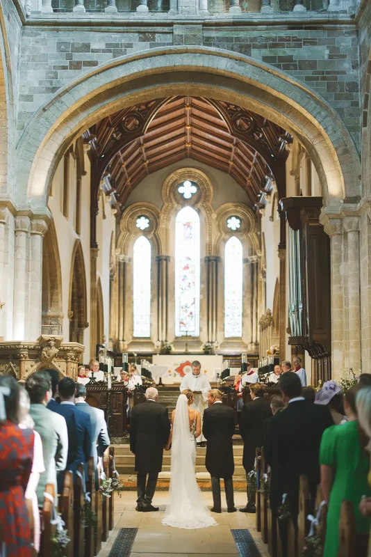 Wide view of wedding ceremony at the altar of Wimborne Minster with guests filling the pews and stained glass windows above