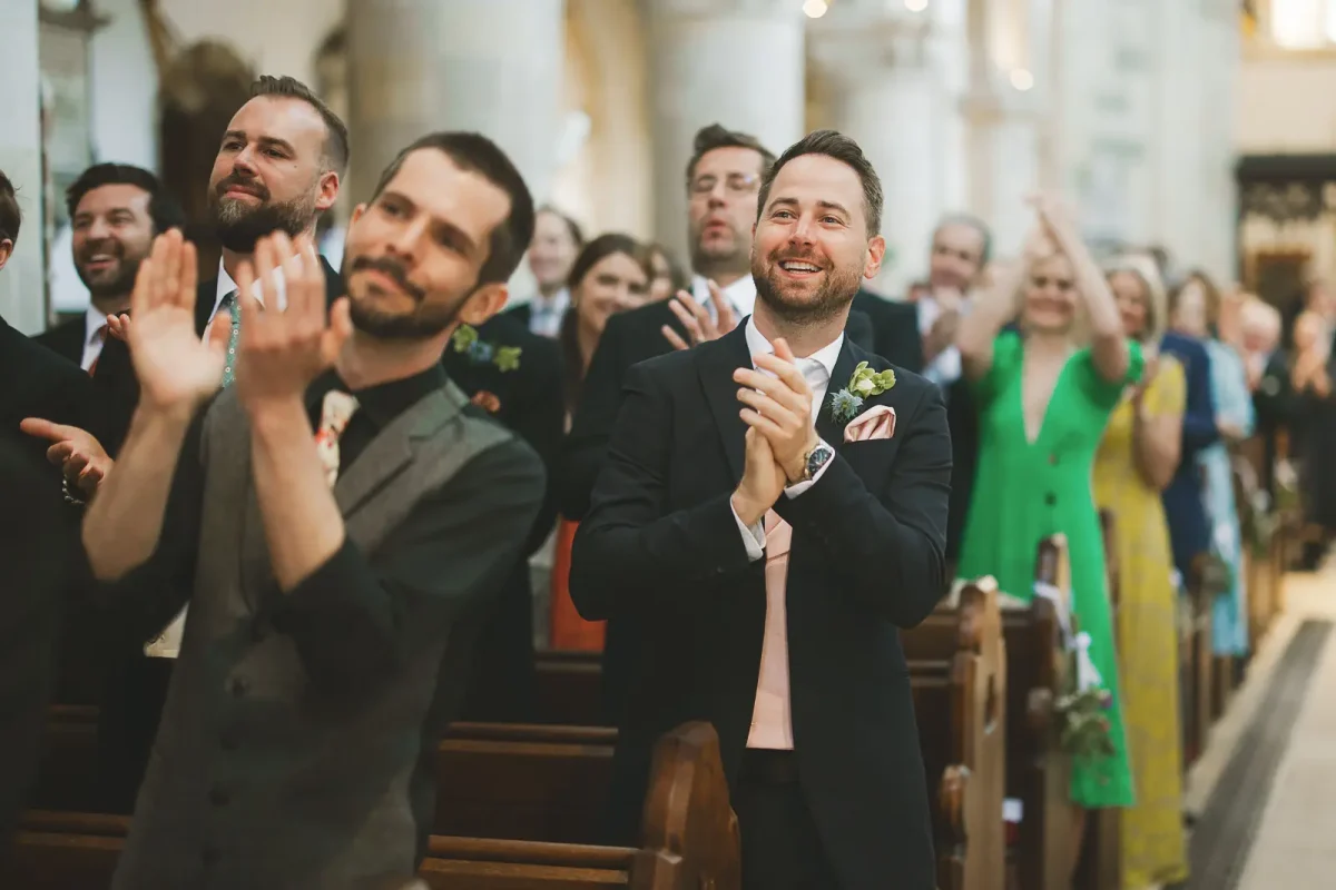 Wedding guests clapping and cheering in the pews of Wimborne Minster church after the couple are pronounced married