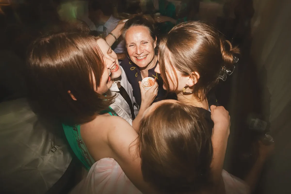 Group of wedding guests hugging and laughing together on the dance floor late into the evening party