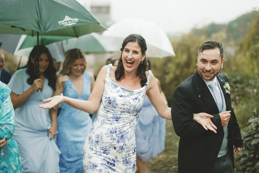 Wedding guests laughing and walking through rain during a wet weather wedding in Dorset