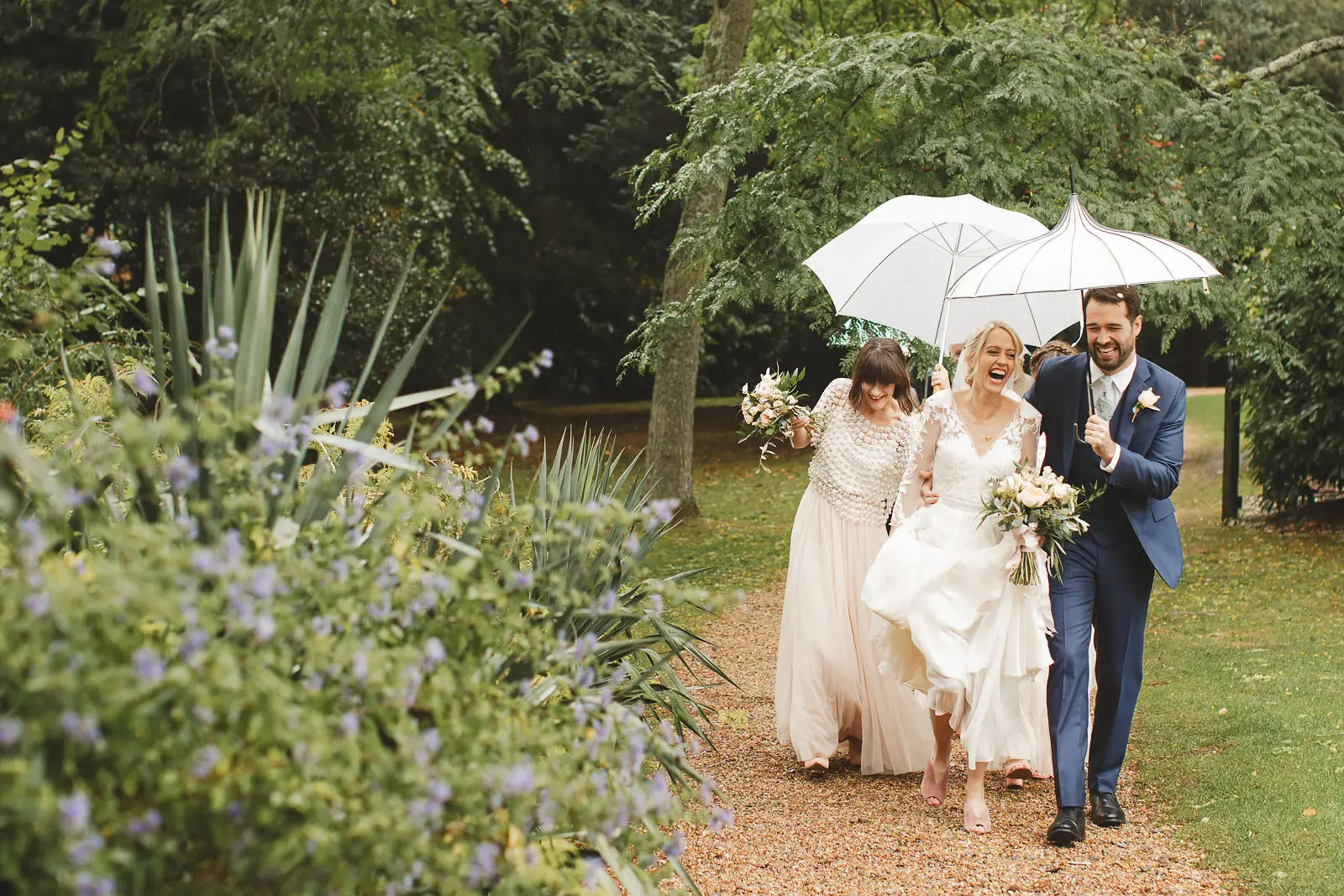 Bride and groom with guests under umbrellas during a wet weather wedding in Dorset