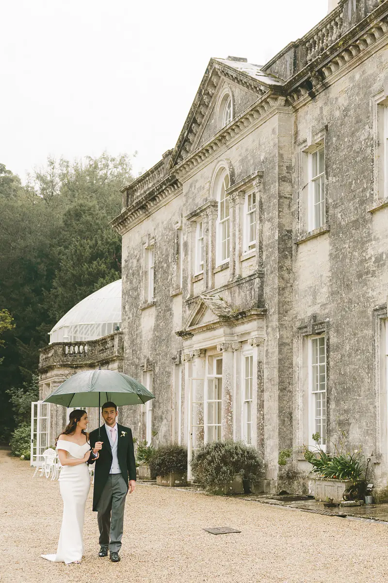 Bride and groom walking under an umbrella during wet weather wedding photography in Dorset
