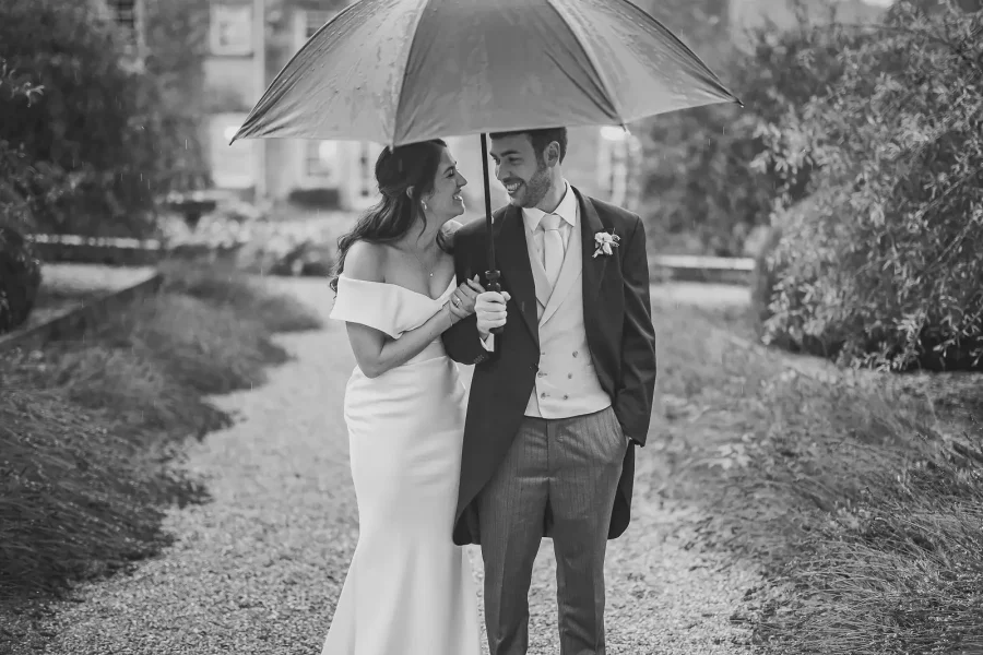 Bride and groom smiling beneath an umbrella during a wet weather wedding portrait in Dorset