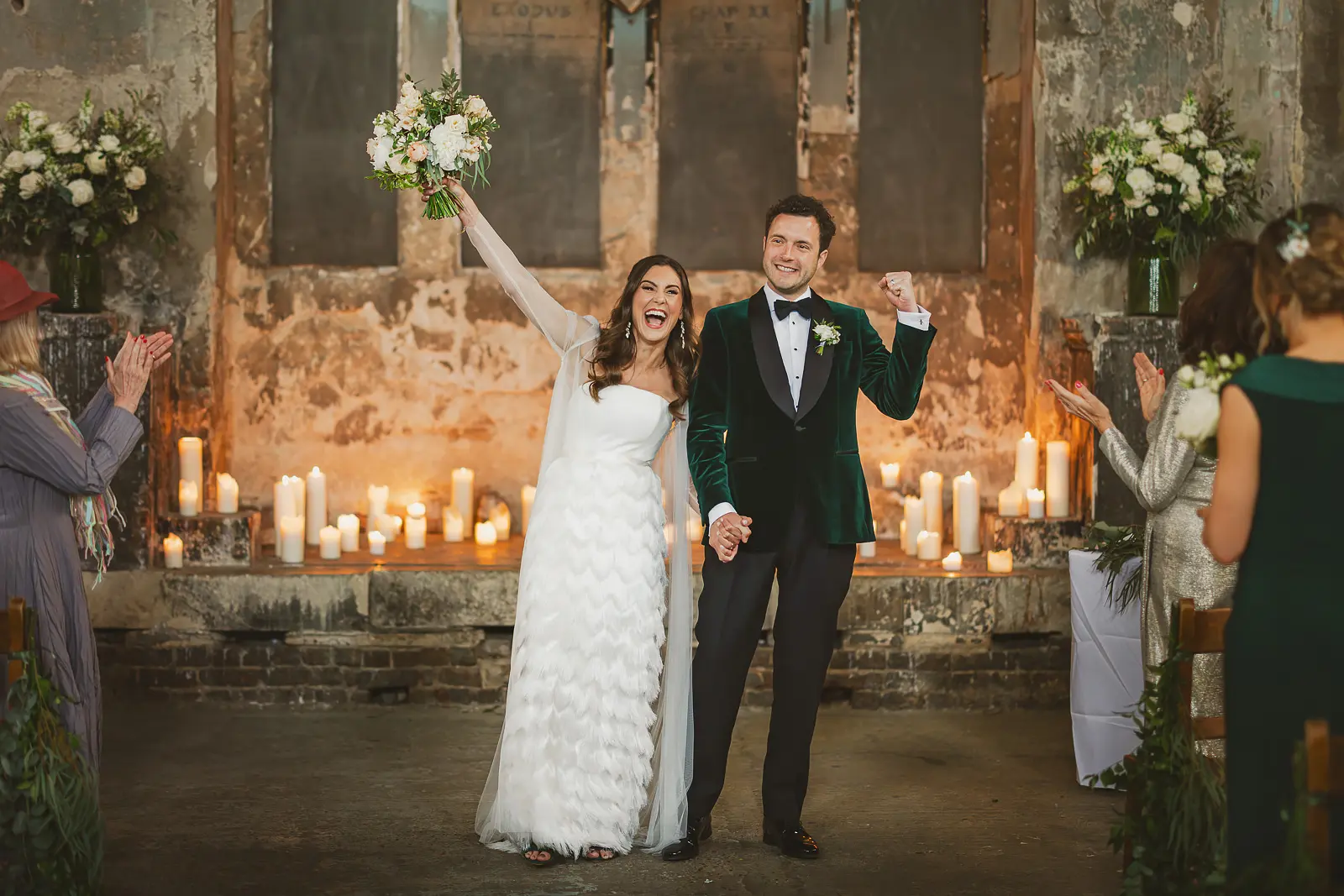 Bride raising her bouquet and groom punching the air in celebration at the altar of the Asylum Chapel London, groom in an emerald green velvet dinner jacket