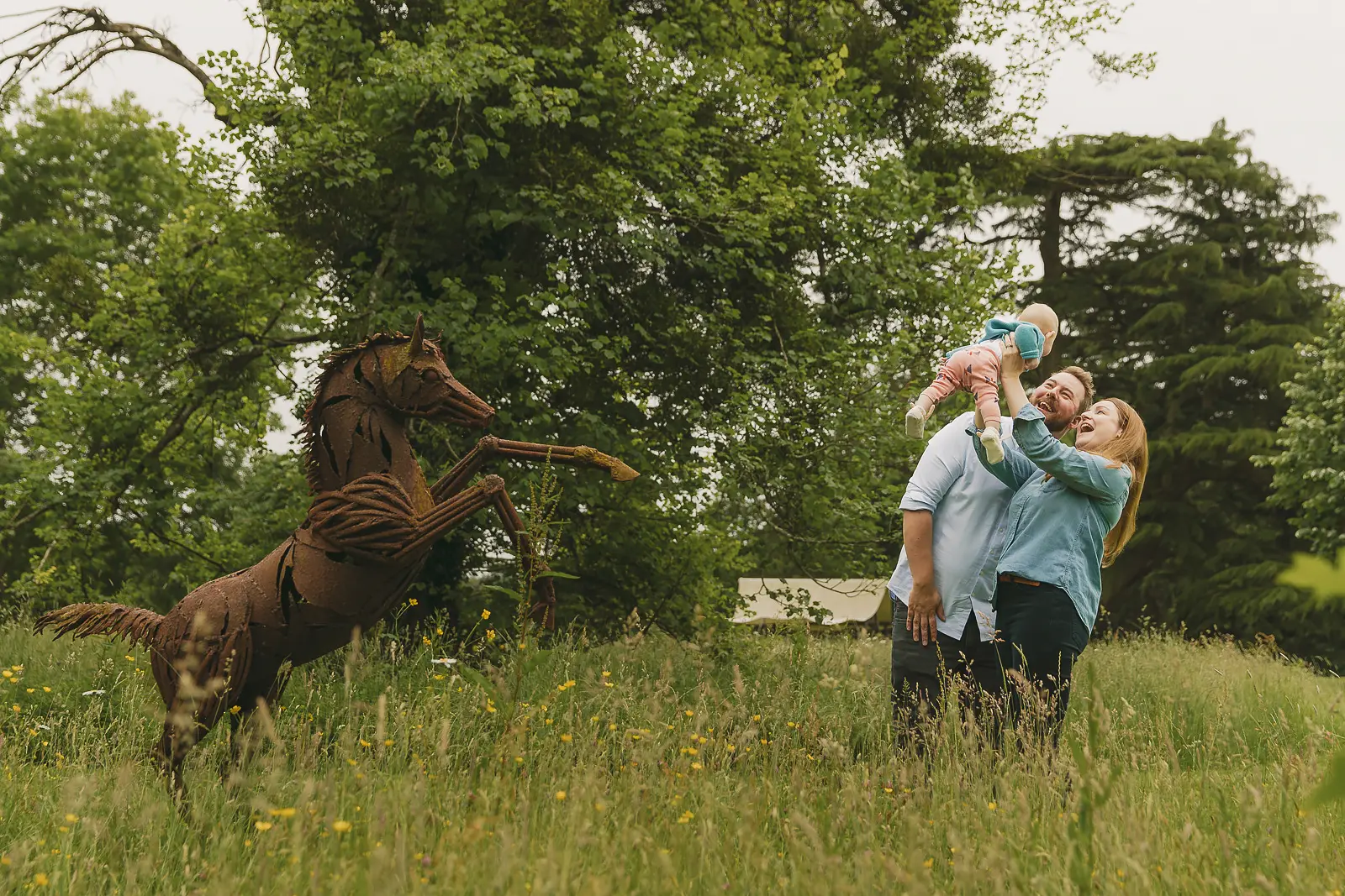 Family photographed during a relaxed woodland shoot in Bournemouth, with parents holding their baby in a meadow.