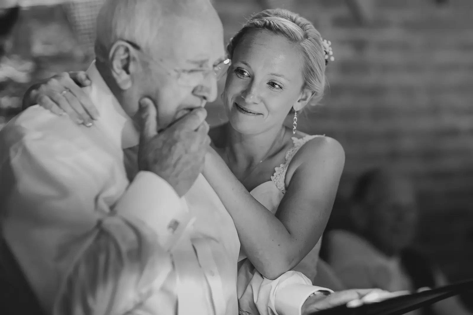 Black and white close-up of bride lovingly embracing her elderly father who is overwhelmed with emotion, hand held to his mouth, at a Dorset wedding ceremony