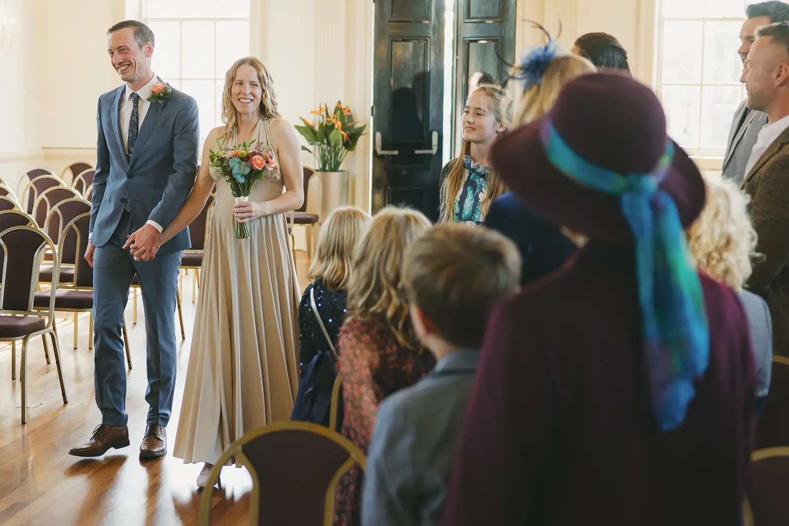 Bride and groom smiling as they enter the ceremony room at Poole Guildhall, guests turning to greet them