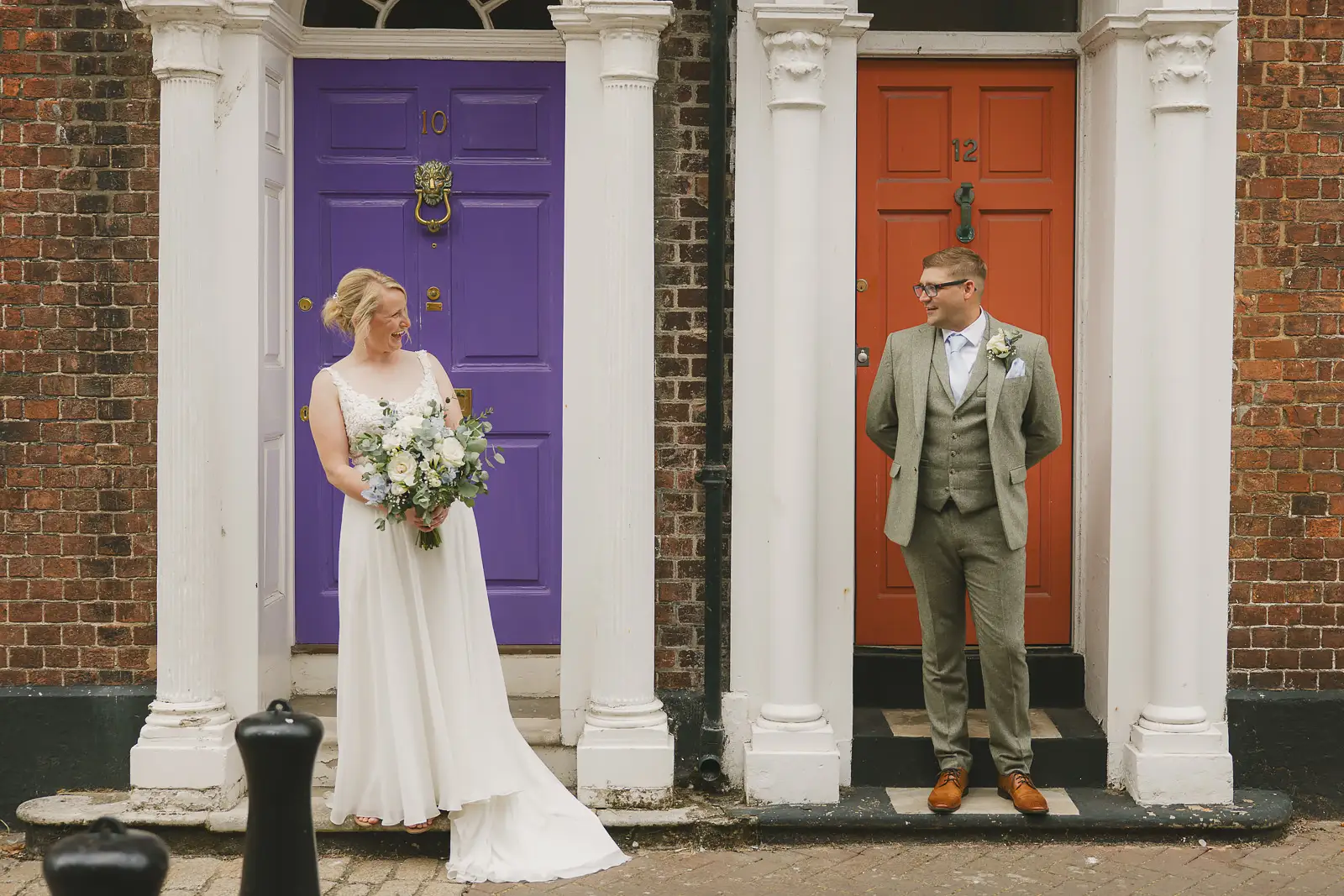 Bride and groom posed before contrasting purple and orange Georgian doors on a Poole Old Town street after their wedding