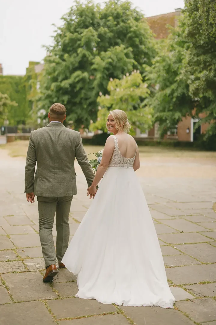 Bride glancing back over her shoulder with a smile as newlyweds walk away across Poole Guildhall grounds on their wedding day