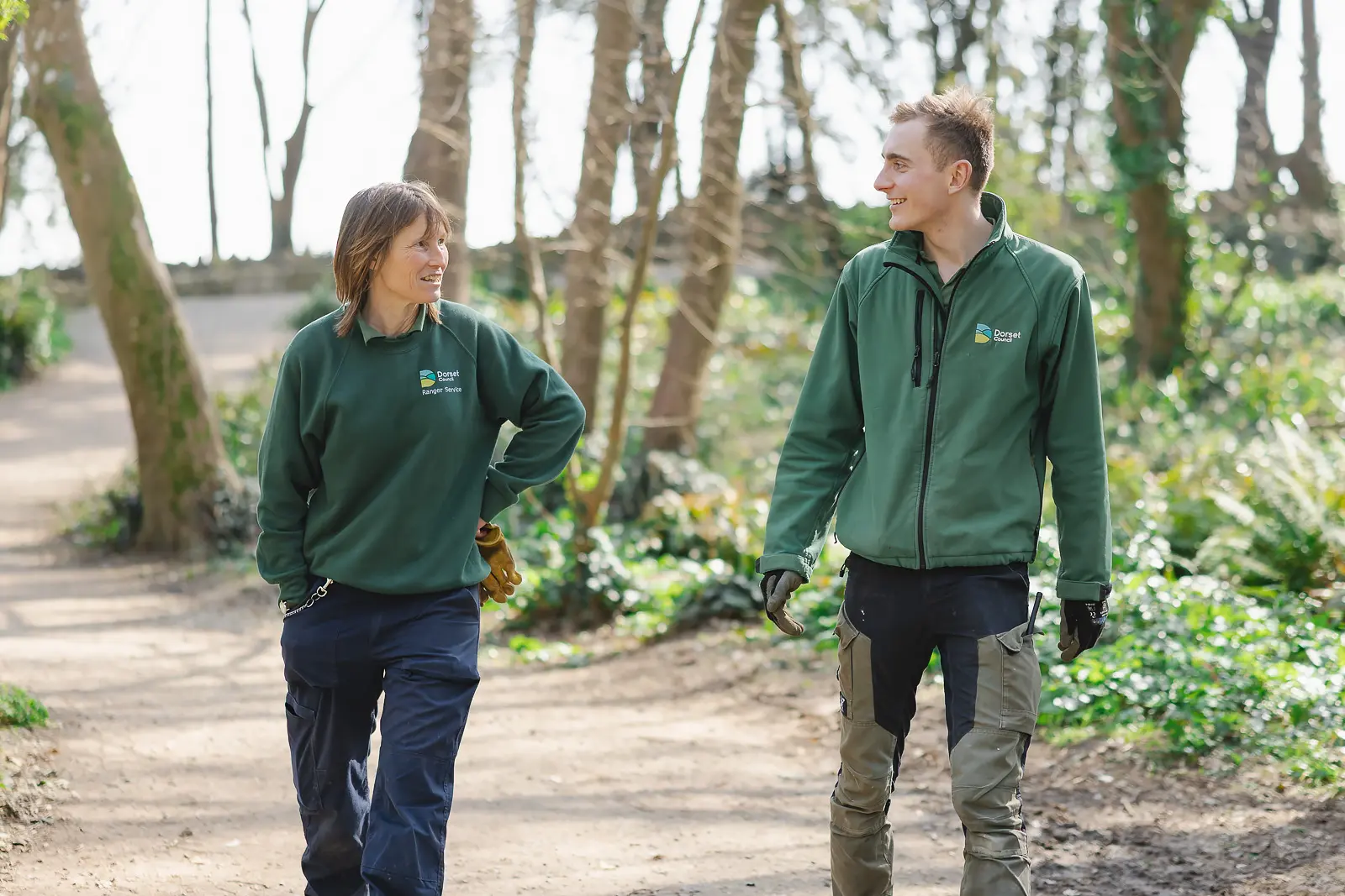 Two grounds team members walking and chatting along a woodland path at Durlston Country Park in Dorset, natural lifestyle photography