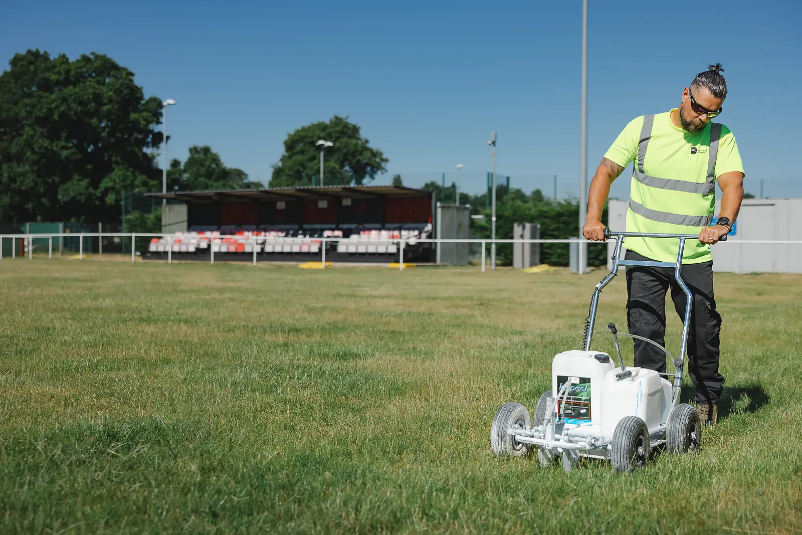 Groundskeeper operating a line-marking machine on a grass sports pitch in Dorset, on-location commercial lifestyle photography