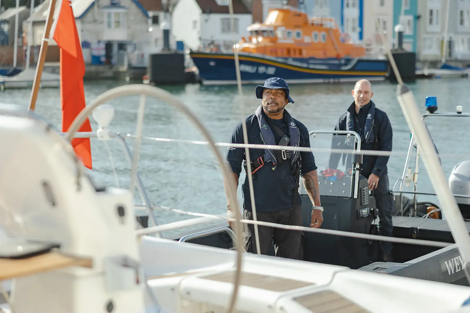 Two harbour team members in life jackets aboard a patrol RIB at Weymouth Harbour with the RNLI lifeboat behind
