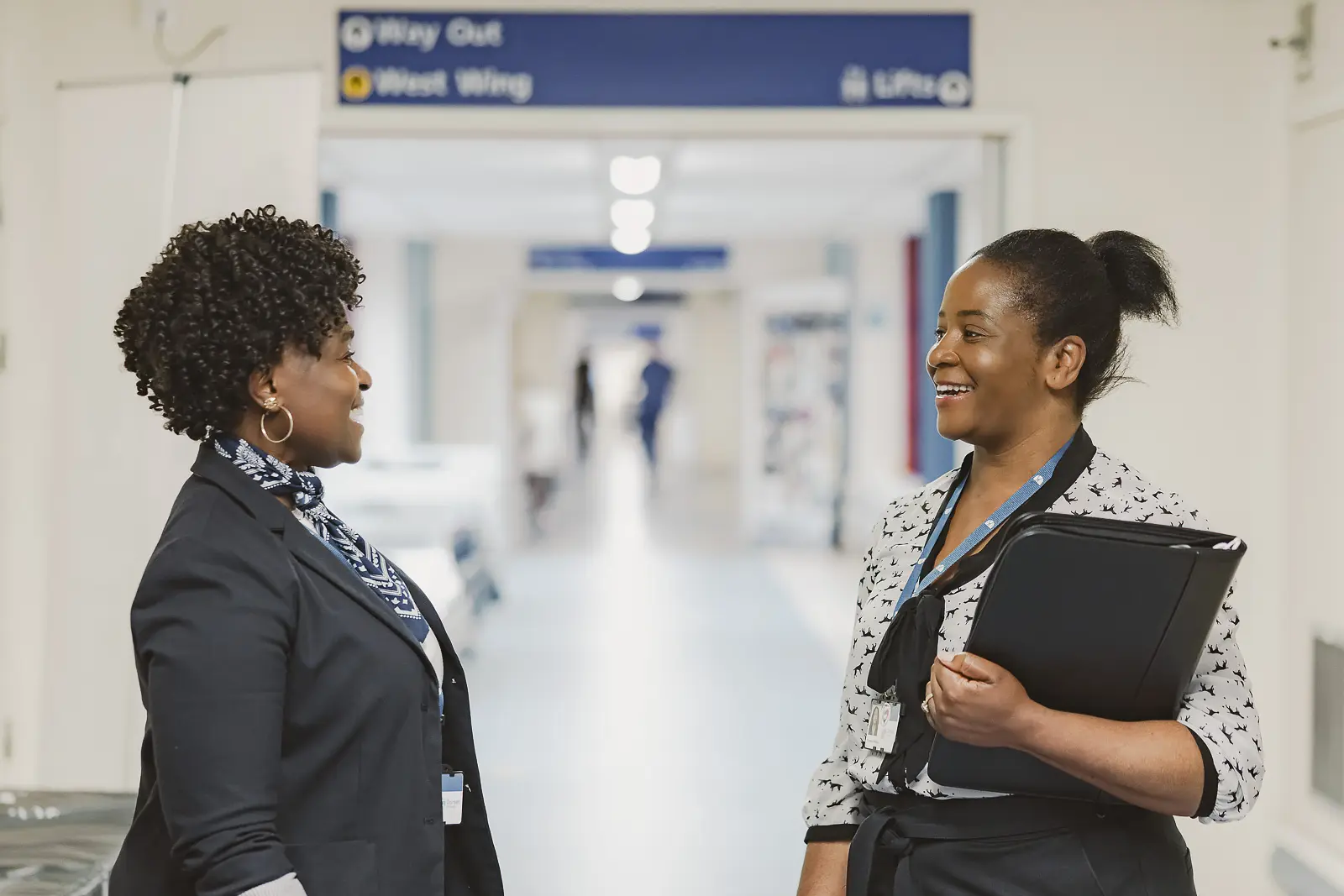 Two healthcare professionals laughing together in conversation in a hospital corridor at Bournemouth, candid and natural