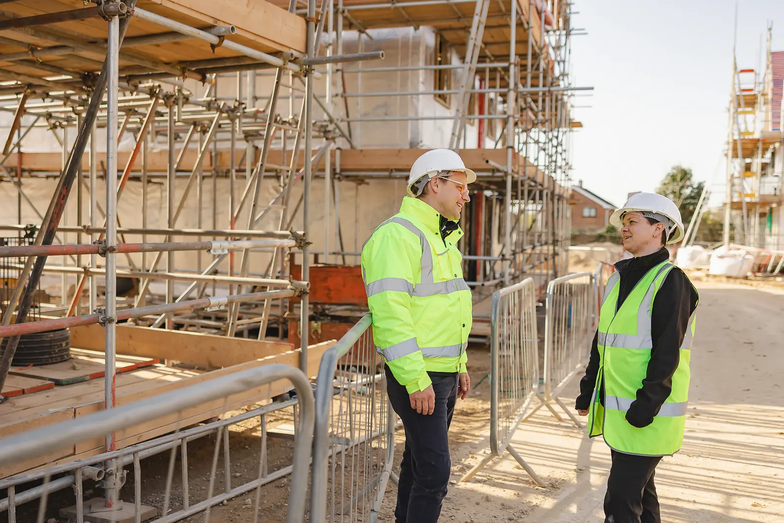 Two planning professionals in hi-vis jackets and hard hats in discussion on a new-build development site at Poundbury, Dorset