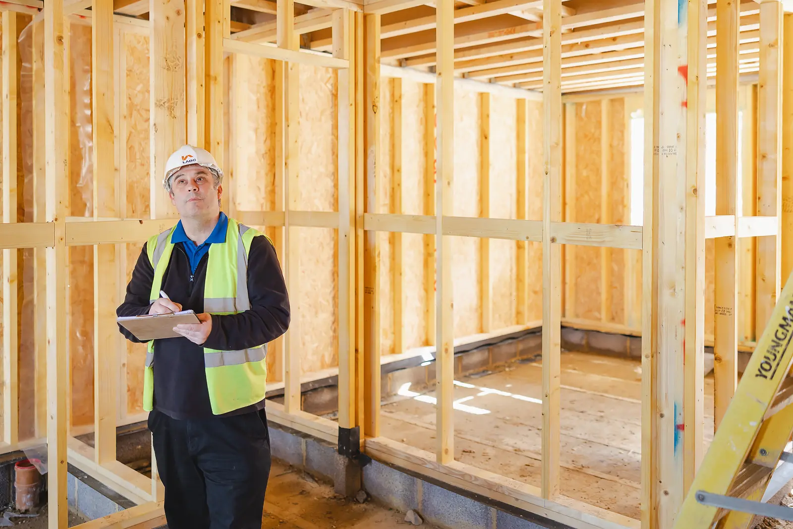 Building inspector writing on a clipboard inside a timber frame new-build property at Poundbury, on-location commercial photography in Dorset