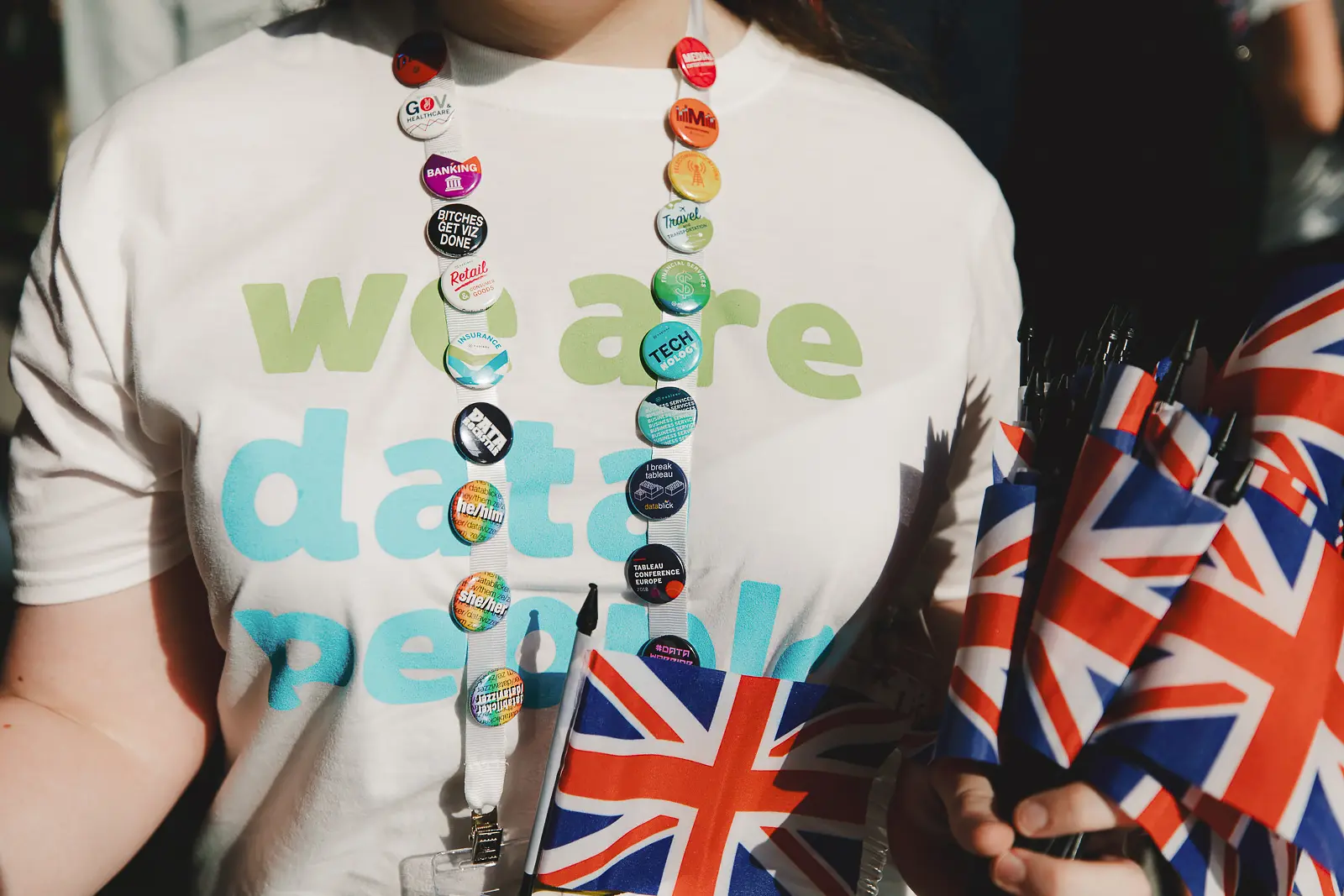 Close-up detail of conference delegate lanyard covered in colourful sector badges holding Union Jack flags at ExCeL London