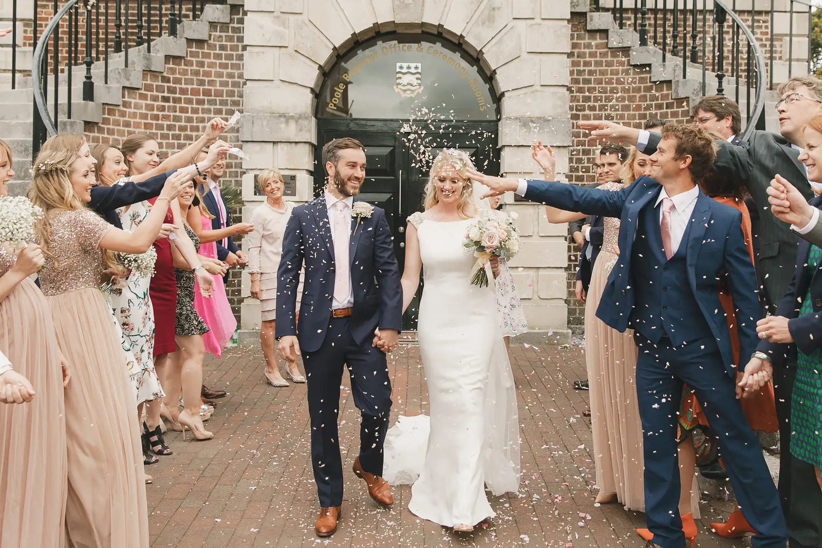Newly married couple walking through confetti outside Poole Guildhall registry office, guests lining the entrance steps