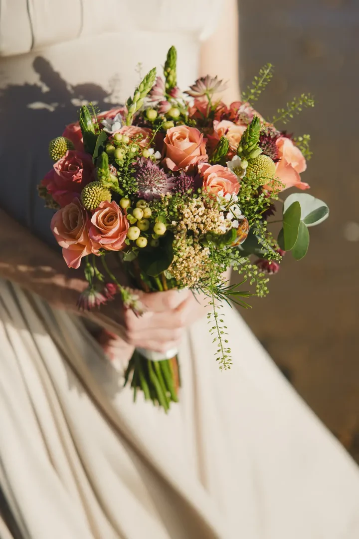 Close-up of bridal bouquet with coral roses, thistles, green berries and eucalyptus at Poole registry office wedding