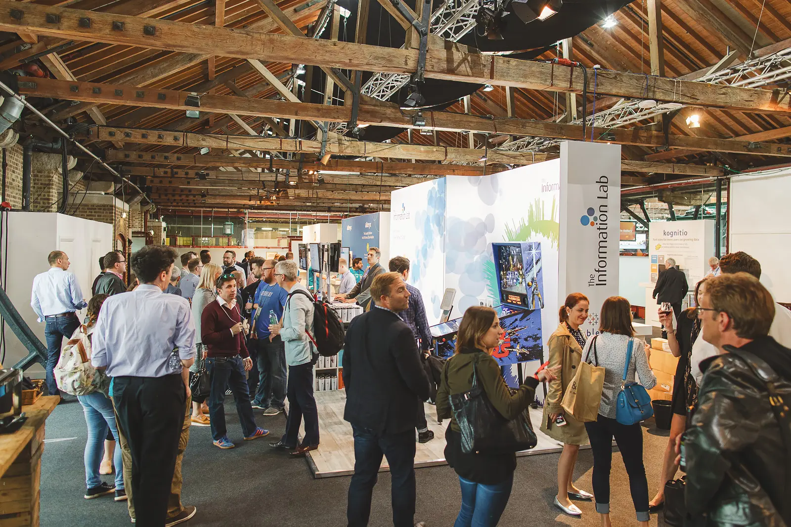 Busy corporate exhibition floor with delegates browsing stands inside Tobacco Dock exposed brick warehouse venue