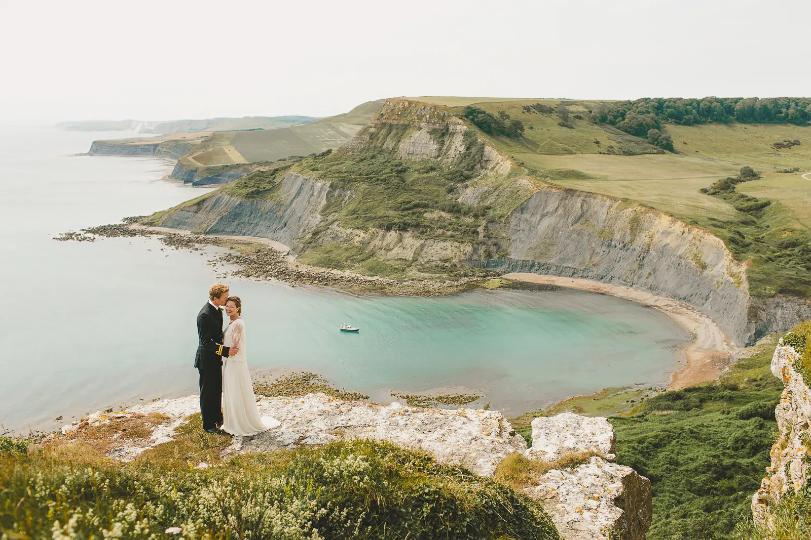Couple embracing on a clifftop overlooking Chapman's Pool, Dorset, with stunning views of the turquoise circular cove and sweeping Jurassic Coast chalk cliffs beyond