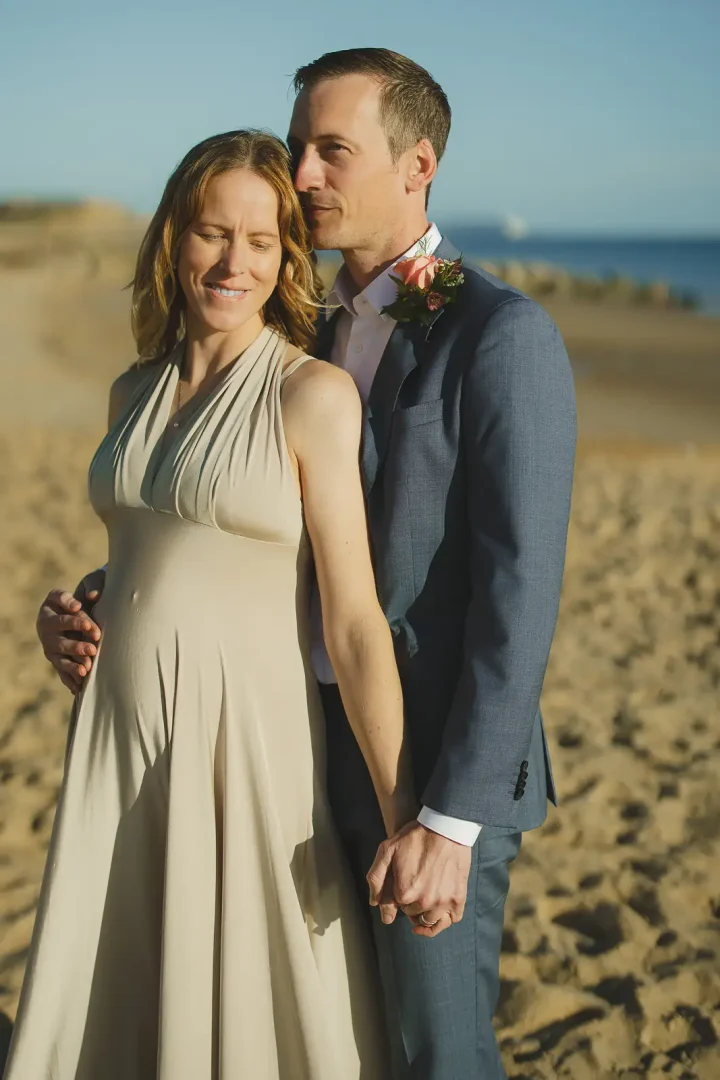 Groom nuzzling bride's hair in warm golden light on a sandy Dorset beach after their Poole registry office wedding