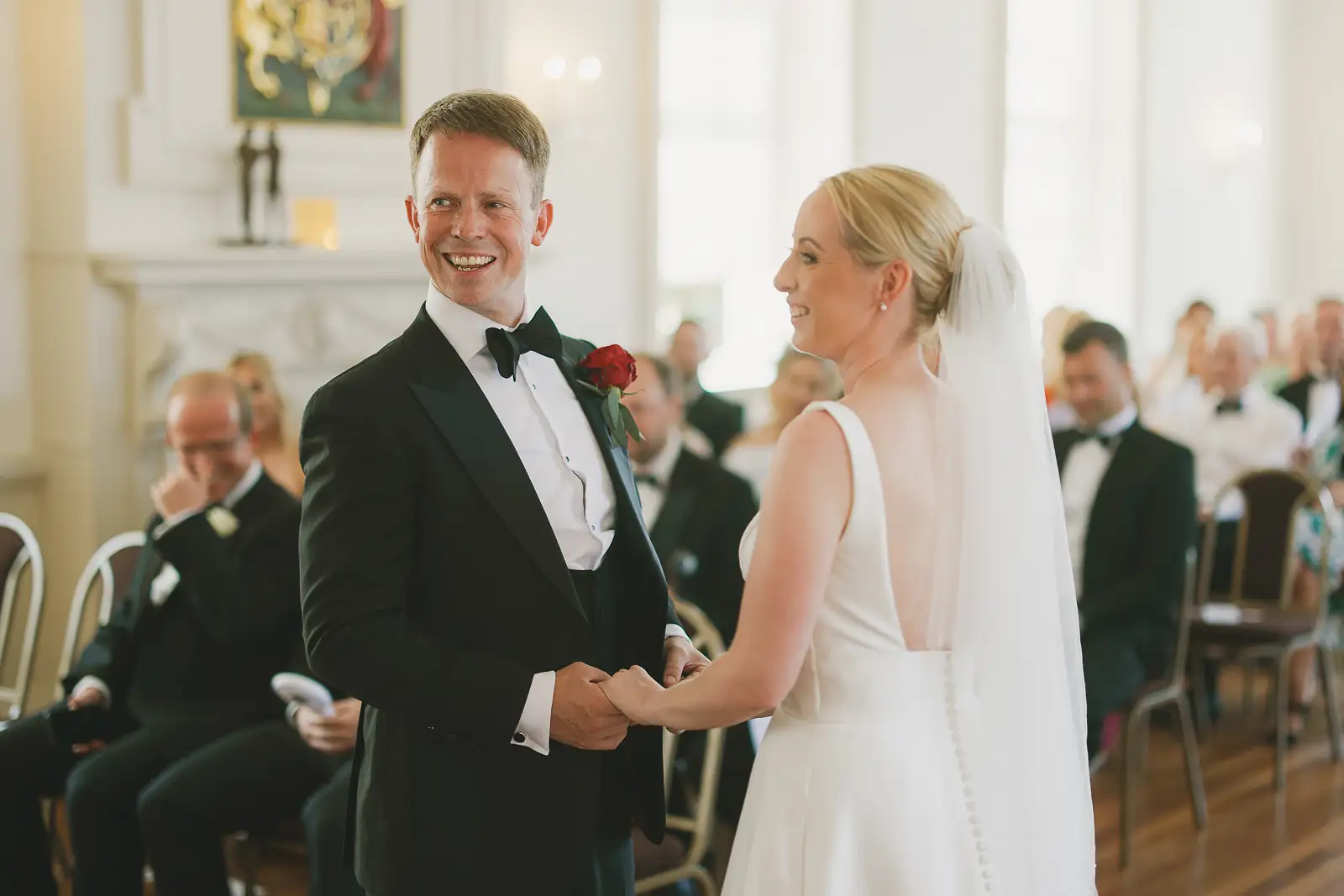 Groom in black tie smiling as he holds his bride's hands during their wedding ceremony inside Poole Guildhall, captured by Poole wedding photographer Paul Underhill