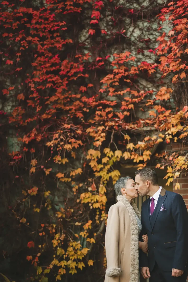 Couple kissing in front of a wall of vivid autumn red and orange foliage after their Poole registry office wedding