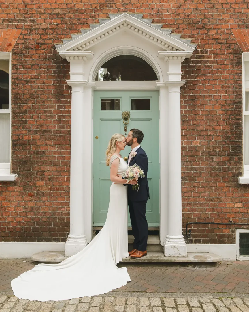 Bride and groom kissing in front of elegant Georgian doorway with sage green door in Poole Old Town after registry office wedding