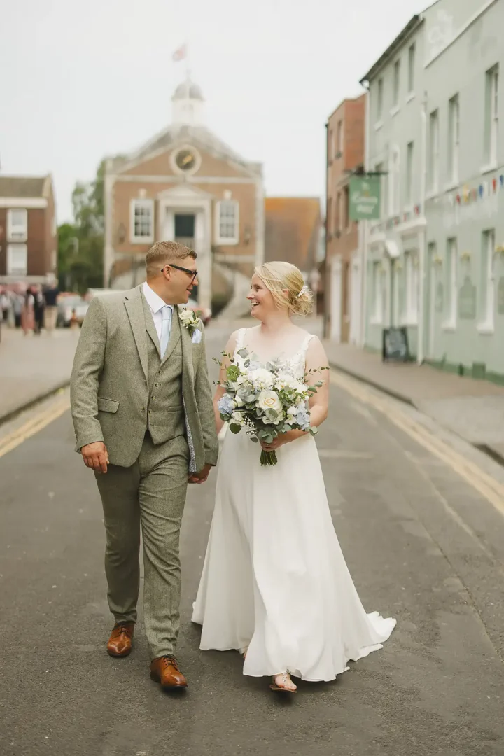 Bride and groom walking hand in hand through Poole Old Town with Poole Guildhall clock tower visible in the background