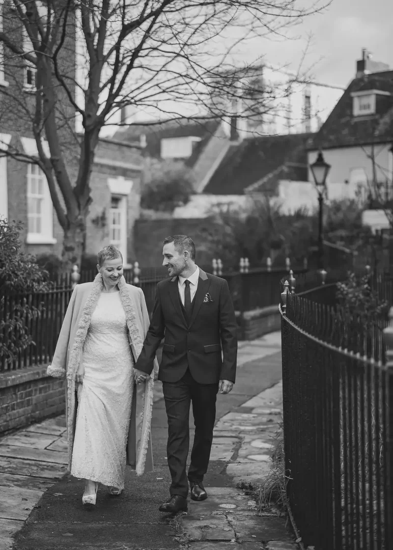 Bride and groom walking hand in hand through Poole Old Town streets in black and white, bare winter trees behind