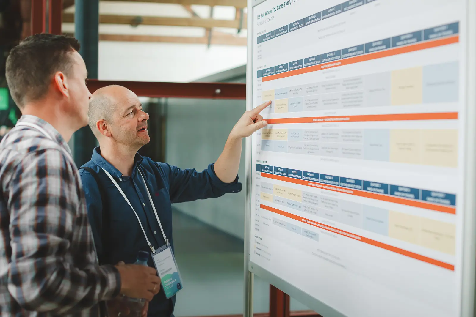 Two conference delegates reviewing multi-day event schedule board at Tobacco Dock London corporate conference