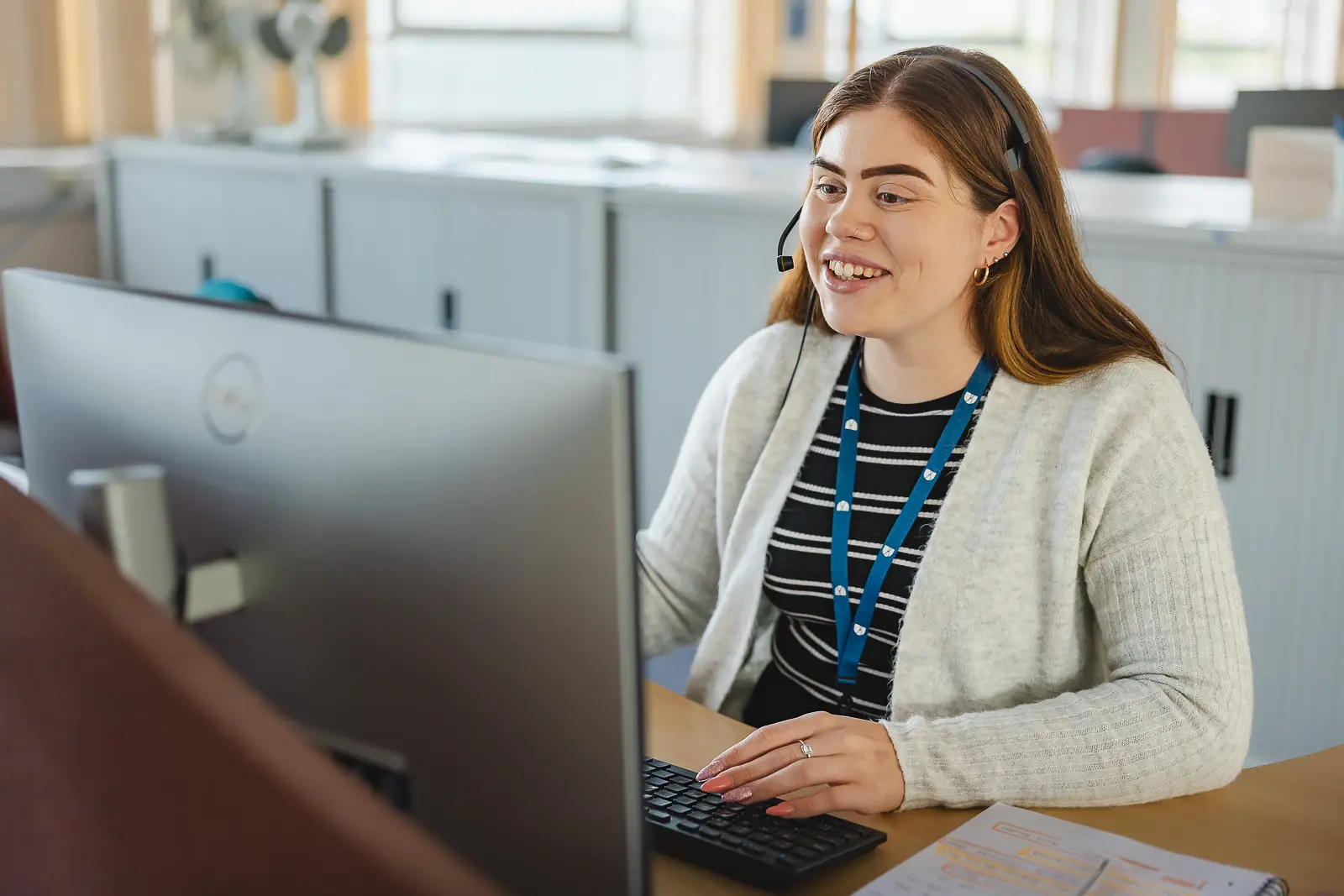 Smiling customer services advisor wearing a headset and working at a computer in a bright Dorset open-plan office
