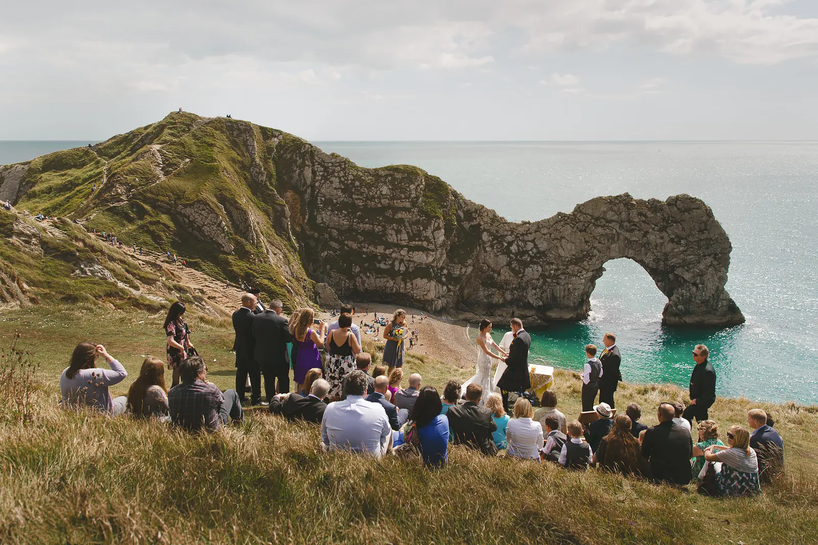Outdoor wedding ceremony on the clifftop above Durdle Door with the iconic limestone arch and turquoise Jurassic Coast sea beyond