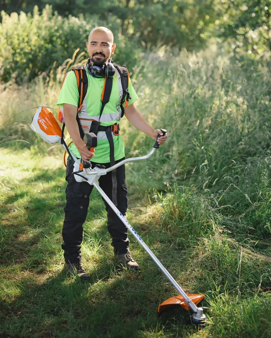 Grounds maintenance worker with a Stihl strimmer in a sunlit meadow at Moors Valley Country Park in Dorset