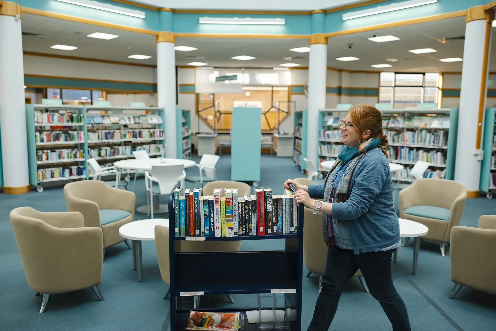 Library staff member pushing a book trolley through a bright open-plan library interior in Dorset