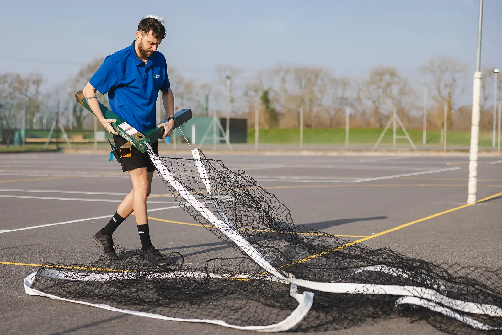 Leisure centre worker setting up a sports net on an outdoor court in Dorset, natural on-location employee lifestyle photograph