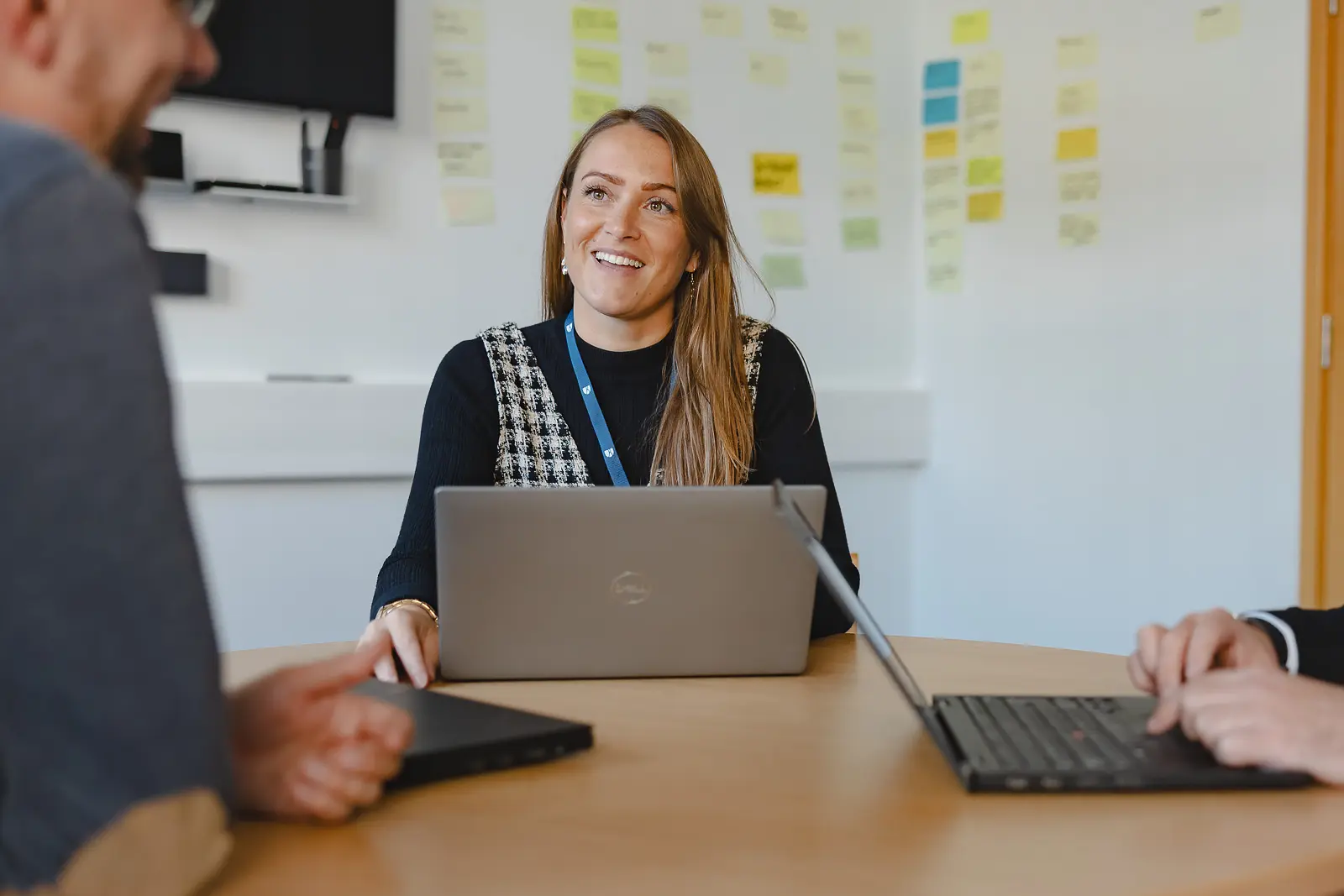 Smiling professional woman at a meeting table with colleagues and a project planning wall covered in sticky notes behind her in Dorchester