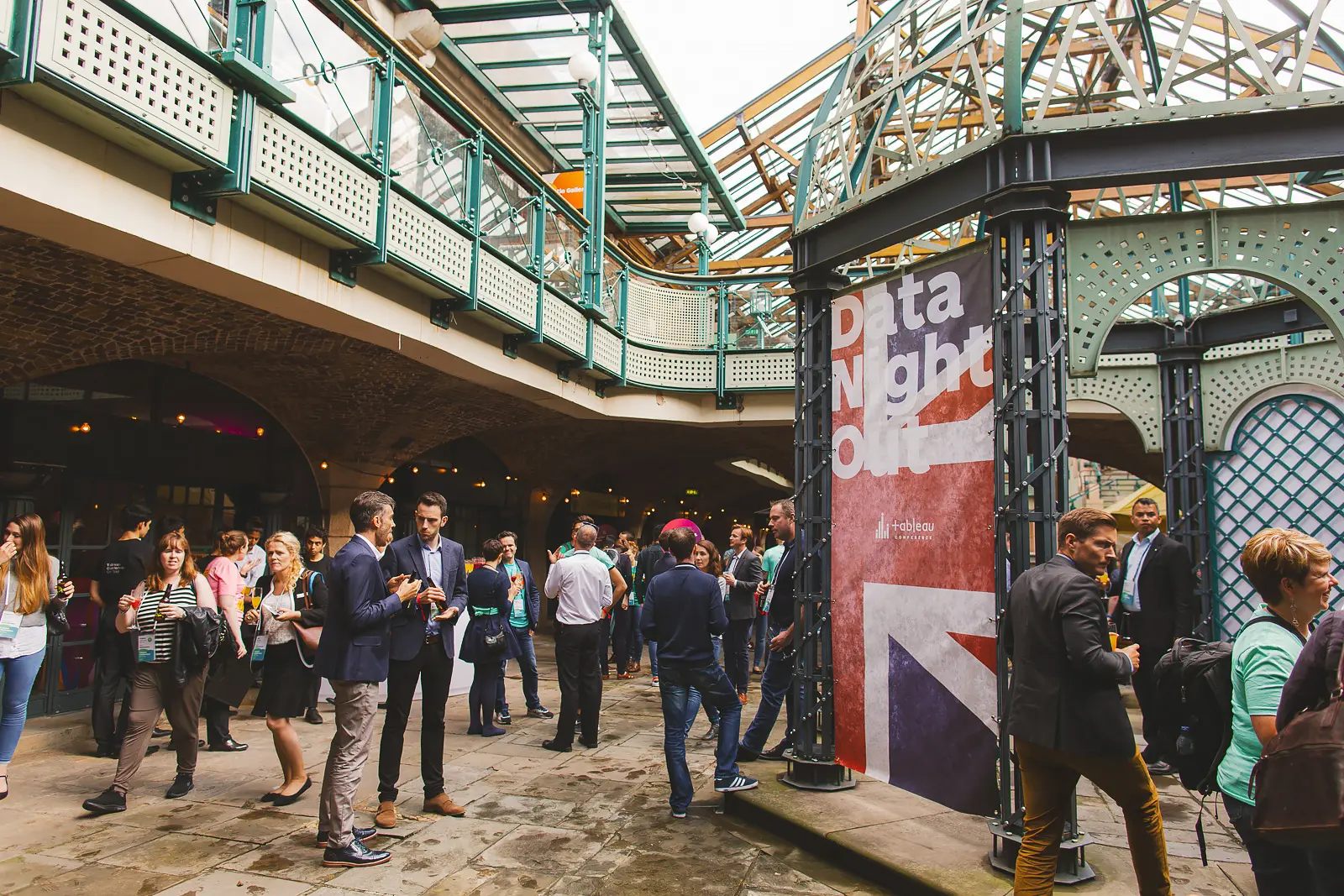 Delegates gathered for evening event in Tobacco Dock outdoor courtyard below ornate green iron gallery structure