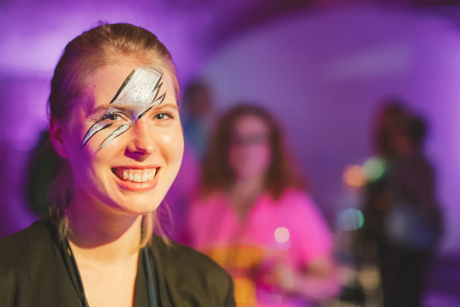 Smiling woman with glitter face paint at corporate evening entertainment event at Tobacco Dock London with purple lighting