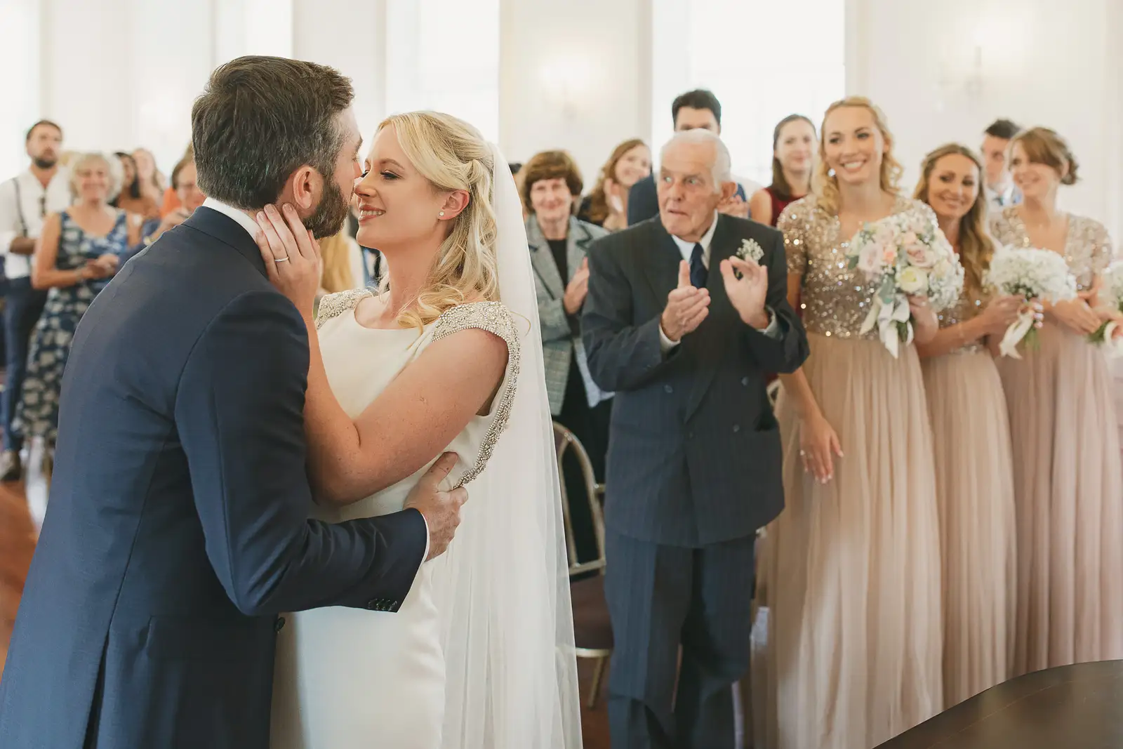 Newlyweds sharing their first kiss as guests and bridesmaids applaud at Poole Guildhall registry office wedding
