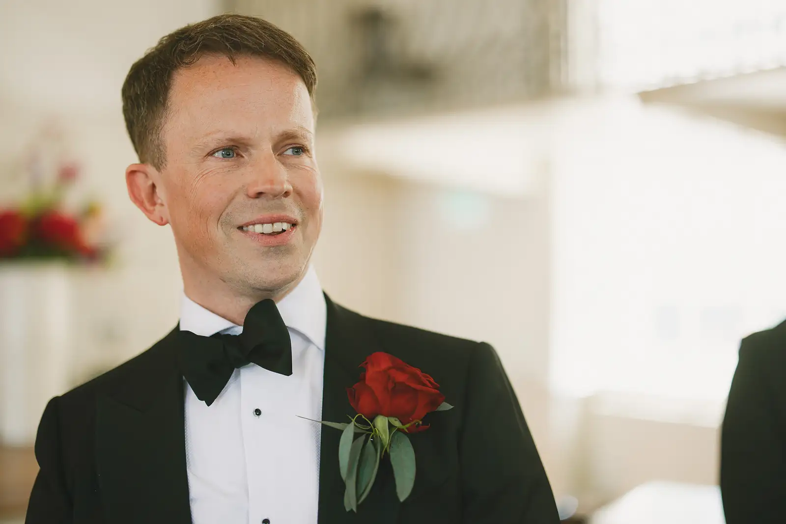 Groom in black tuxedo with red rose buttonhole smiling as he waits for his bride at Poole Guildhall registry office ceremony
