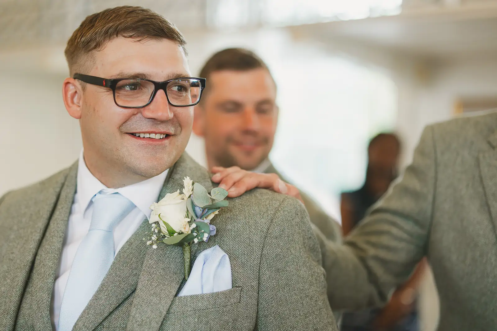 Groom smiling warmly with best man's hand on his shoulder while waiting for bride at Poole Guildhall registry office