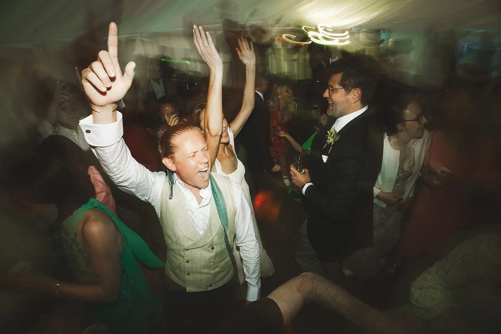 Exuberant wedding reception dancing with motion blur as guests throw their arms up and celebrate at a packed dance floor late into the evening